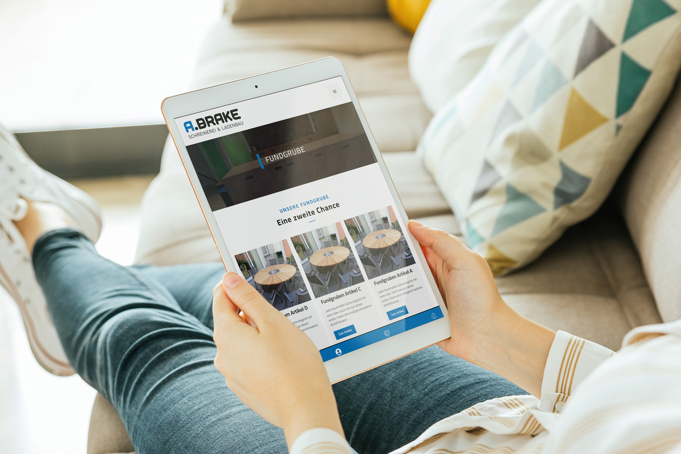 Person, die ein Tablet auf einem Sofa hält, mit einer Website von A. Brake sichtbar.